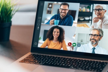 A imagem apresenta um notebook enquanto ocorre uma chamada de vídeo de trabalho. Na tela aparecem quatro pessoas.